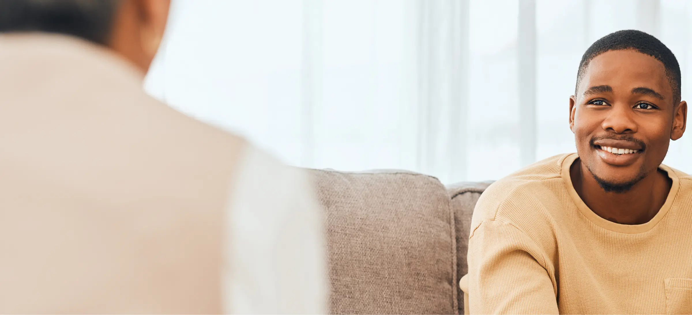 A hopeful African American man smiles while looking toward his partially unseen therapist.