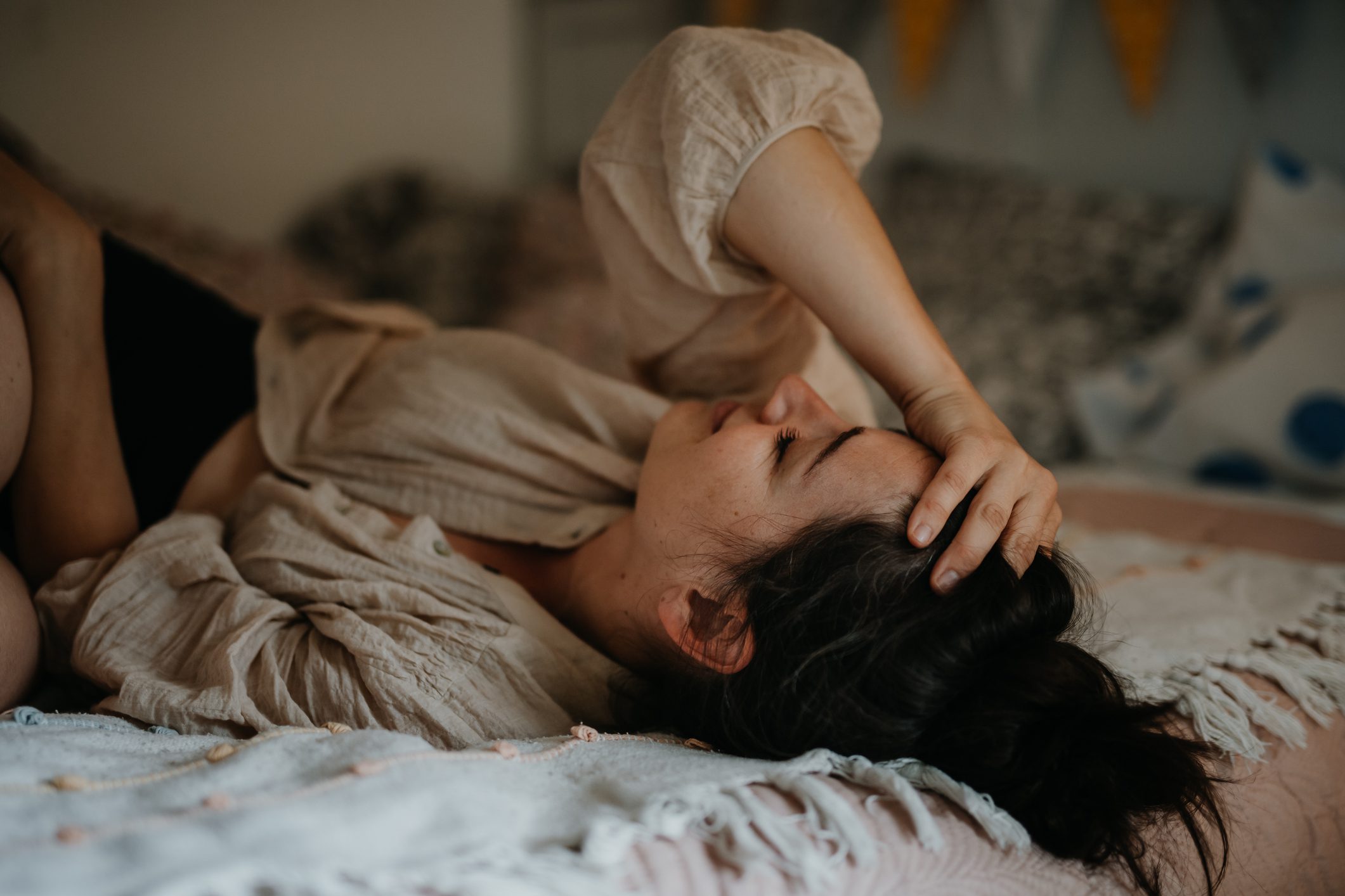 A woman holds her head while laying on her bed stressed