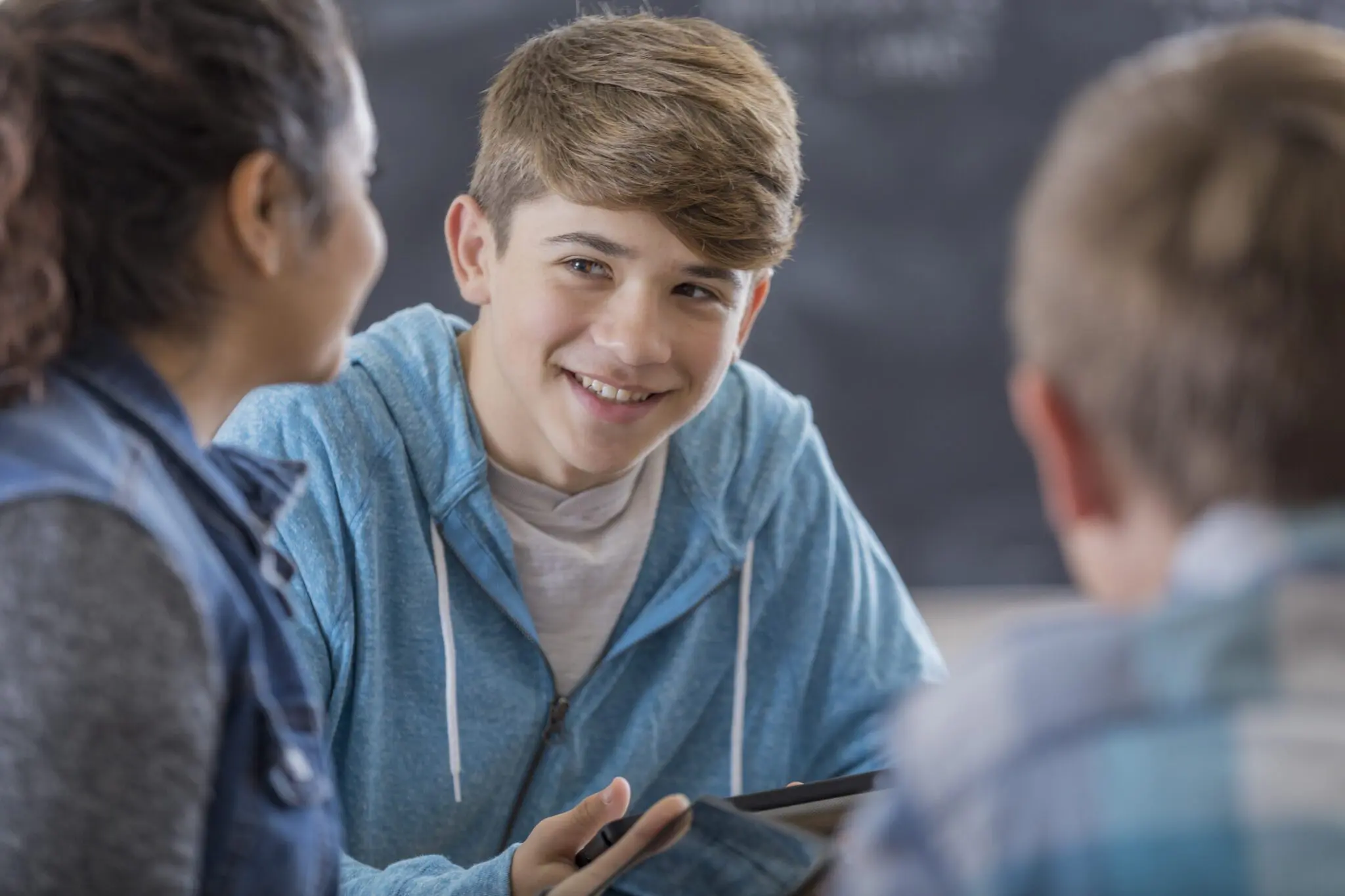 A teen boy smiles while hanging out with his friends in school